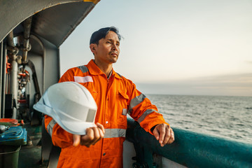 Filipino deck Officer on deck of vessel or ship , wearing PPE personal protective equipment - helmet, coverall, lifejacket, goggles. Safety and work at sea. - obrazy, fototapety, plakaty