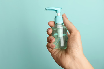 Woman holding antiseptic gel on light blue background, closeup