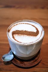 A ceramic white artisenal cup with foamed milk and sprinkled cinnamon at the top, on the wooden table.