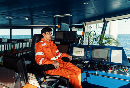 Filipino deck Officer on bridge of vessel or ship wearing coverall during navigaton watch . He is looking forward. COLREG. Sea is on background