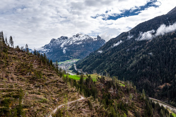 Fototapeta na wymiar Aerial view of valley with green slopes of the mountains of Italy cloudy weather, Trentino, The trees tumbled down by a wind, huge clouds over a valley, green meadows, Dolomites on background