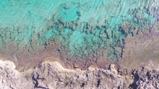 AERIAL DRON TOP DOWN STILL SHOT OF ROCKY COST AND SAND WITH TURQUOISE TRANSPARENT MEDITERRANEAN WATER 