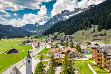 Fototapeta premium Aerial view of valley with Chalet, green slopes of the mountains of Italy, Trentino, Fontanazzo, huge clouds over a valley, roofs of houses of settlements, green meadows, Dolomites on background,