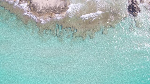 AERIAL DRON TOP DOWN STILL SHOT OF TURQUOISE TRANSPARENT MEDITERRANEAN WATER WITH COAST ROCKS AND SAND