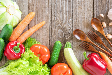 Assorted vegetables, forks and spoons on a wooden background.