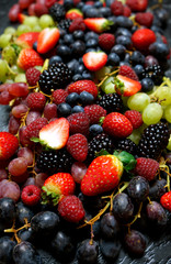 Summer berries food background full frame close up with strawberries, blackberries, blueberries, red, dark and green grapes on black marble.