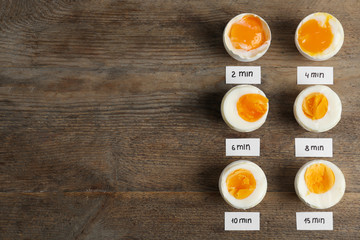 Different cooking time and readiness stages of boiled chicken eggs on wooden table, flat lay. Space for text