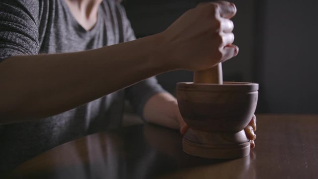 Close up of woman's hands using a mortar and pestle in a dimly-lit room