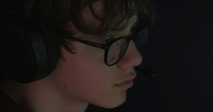 Teenager wears headset to play video game in dark room, close-up