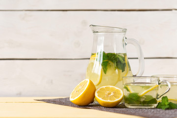 Lemonade with lemon and mint in a jug on a yellow rustic table.