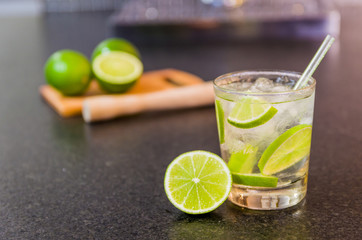Caipirinha, traditional Brazilian alcoholic drink, typical drink made with sugar, lemon, distilled cane (cachaca) and ice. Ingredients and the drink on black granite surface.