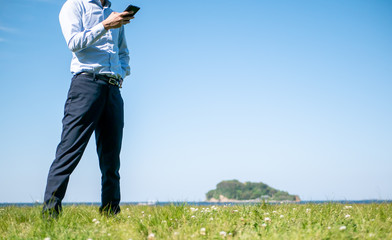 草原でビジネスマンがスマートフォンを操作している