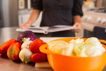 Young woman reading recipe book with fresh vegetables on the table - healthy food - vegetarian food - recipes at home