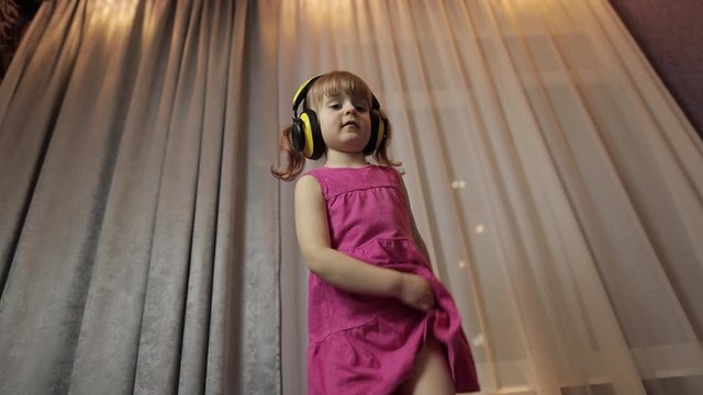 Little child girl in wireless headphones enjoying listen music. Dancing at home