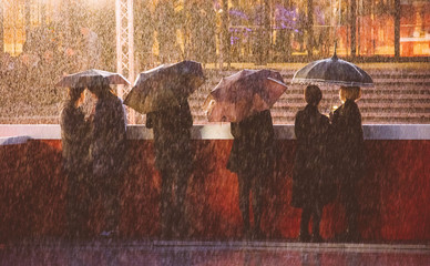 People Standing With Umbrellas By Wall On Rainy Day