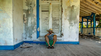 Fototapeta na wymiar A man sitting on the patio of an old decayed house on a tropical beach.