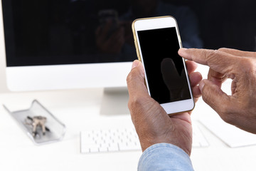Work from Home Concept. Closeup of a man holding his cell phone in front of his desktop computer. Both devices have black screens.