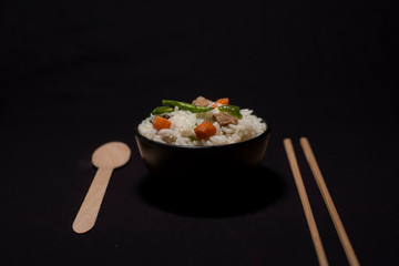 A bowl of rice with vegetables and soya chunks along with chopsticks and spoon in a black copy space background. Food photography.