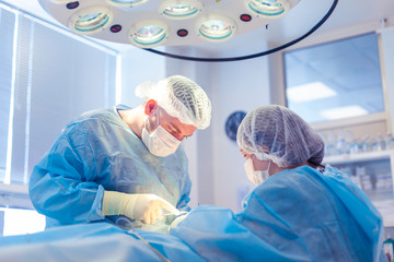 A group of surgeons works in the operating room. Two doctors perform surgery on a patient