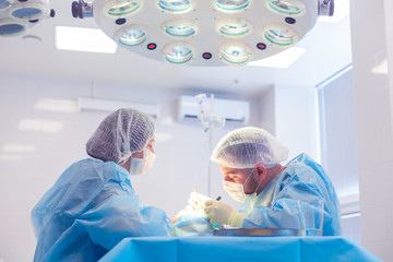 Male surgeon performs surgical procedures in the operating room, while his assistant monitors the...