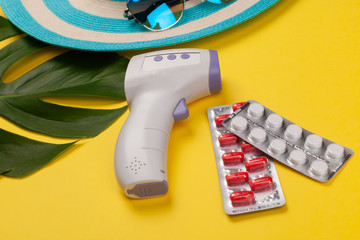 Top view on infrared thermometer, white and red pills in blister pack, blue hat, sunglasses,...