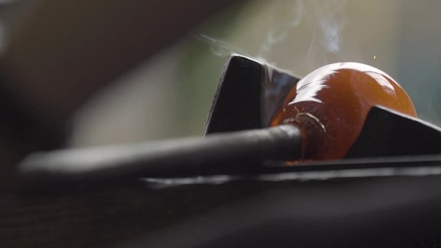 Marvering a red, smoky molten glass on a metal counter, slow motion, craftsmanship
