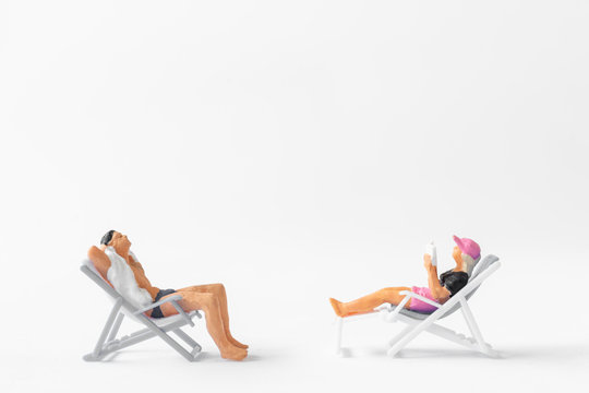 Miniature People Sunbathing On Deck Chairs On White Background , Summer Time Concept