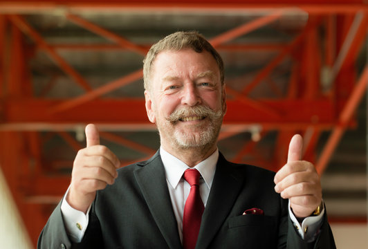 Portrait of old bearded caucasian man in suit gesturing thump upl over studio background,Happy portrait of smiley senior business man with beard and moustache at office.Successful retired man.