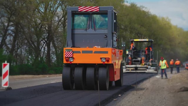 Roller machines make new asphalt roads. The asphalt paver squeezes hot asphalt.