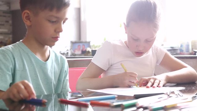 Boy and girl, brother and sister draw a rainbow with crayons together, sitting at a table. Video