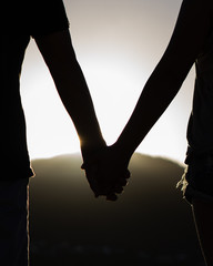 silhouetted holding hands against a sunset