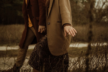 Couple in autumn clothes walks in the field. Hand touching dry grass.