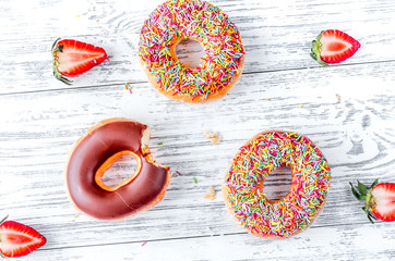 sweet colorful donuts with topping on wooden desk background top view