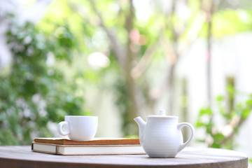 White tea kettle and white cup with notebook on wooden table outdoor view