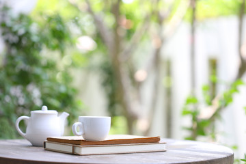 White tea kettle and white cup with notebook on wooden table outdoor view