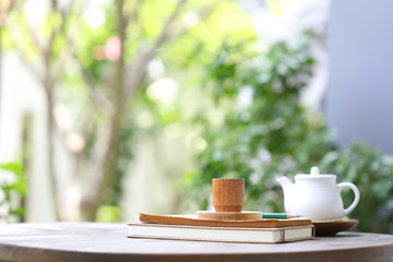 White tea kettle and brown wooden  cup with notebook on wooden table outdoor view