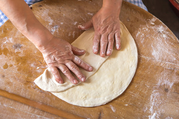 Woman in a black chef's apron roll out the dough for preparing Turkish pancake. 
Woman rolls out dough, close-up. Making Turkish traditional flat cakes.