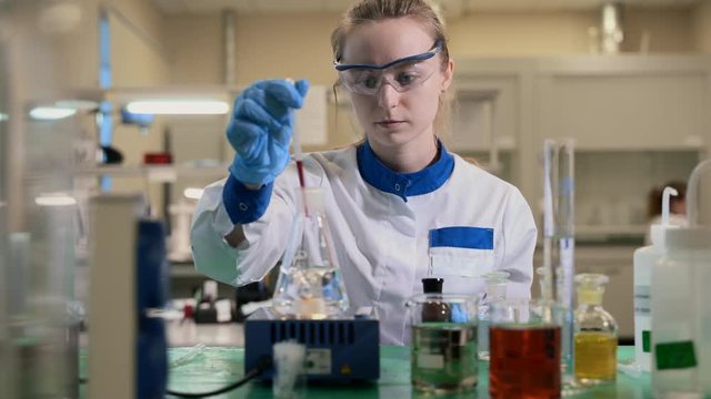 chemist worker pouring a drop of red liquid into beaker with water. mixing and reaction spbas . concept expertise, examine, study. scientist pour liquid using pipette.