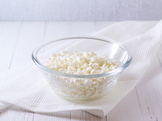 Cottage cheese. Fresh natural cottage cheese in a glass cup stands on a light table, horizontal orientation, there is a place for copying.