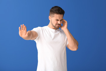Young man suffering from loud noise on color background