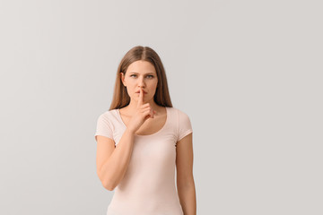 Young woman showing silence gesture on light background