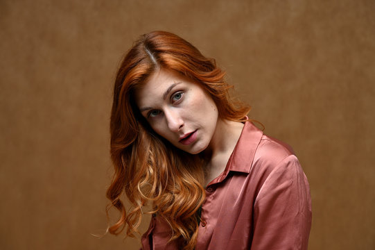 A pretty model is wearing a red shirt. Portrait of actress caucasian woman with red hair showing serious emotions. Photo taken in the studio on a beige background.