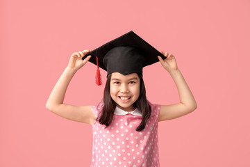 Little girl in graduation hat on color background
