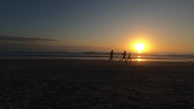 Family running on beach shoreline while beautiful sun rises in the background.