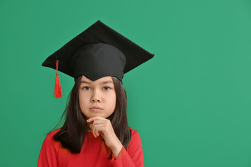 Little girl in graduation hat on color background