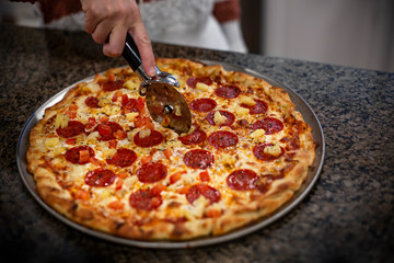 Close up view of a homemade pizza pie. Hand slicing a slice of pizza. Selective focus on the delicious cheesy pizza on a kitchen counter