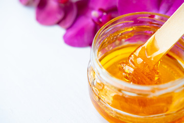 depilation and beauty concept - sugar paste or wax honey for hair removing with wooden waxing spatula stick in jar on flower background. copyspase.