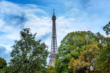 Fototapeta na wymiar Eiffel Tower in the dense green of trees against a bright blue cloudy sky. Postcard. Space for text.