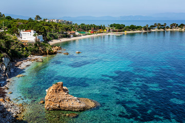 Fototapeta premium A large stone in the form of a heart in the turquoise blue sea and the green shore on a bright sunny day. Great view of the beautiful bay. Relax and tranquility. Postcard. Space for text.