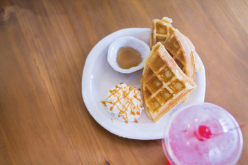 Smooth Focus and Blurred images,Waffles and Maple syrup are placed on a white plate with cream topping to add flavor to the waffles.